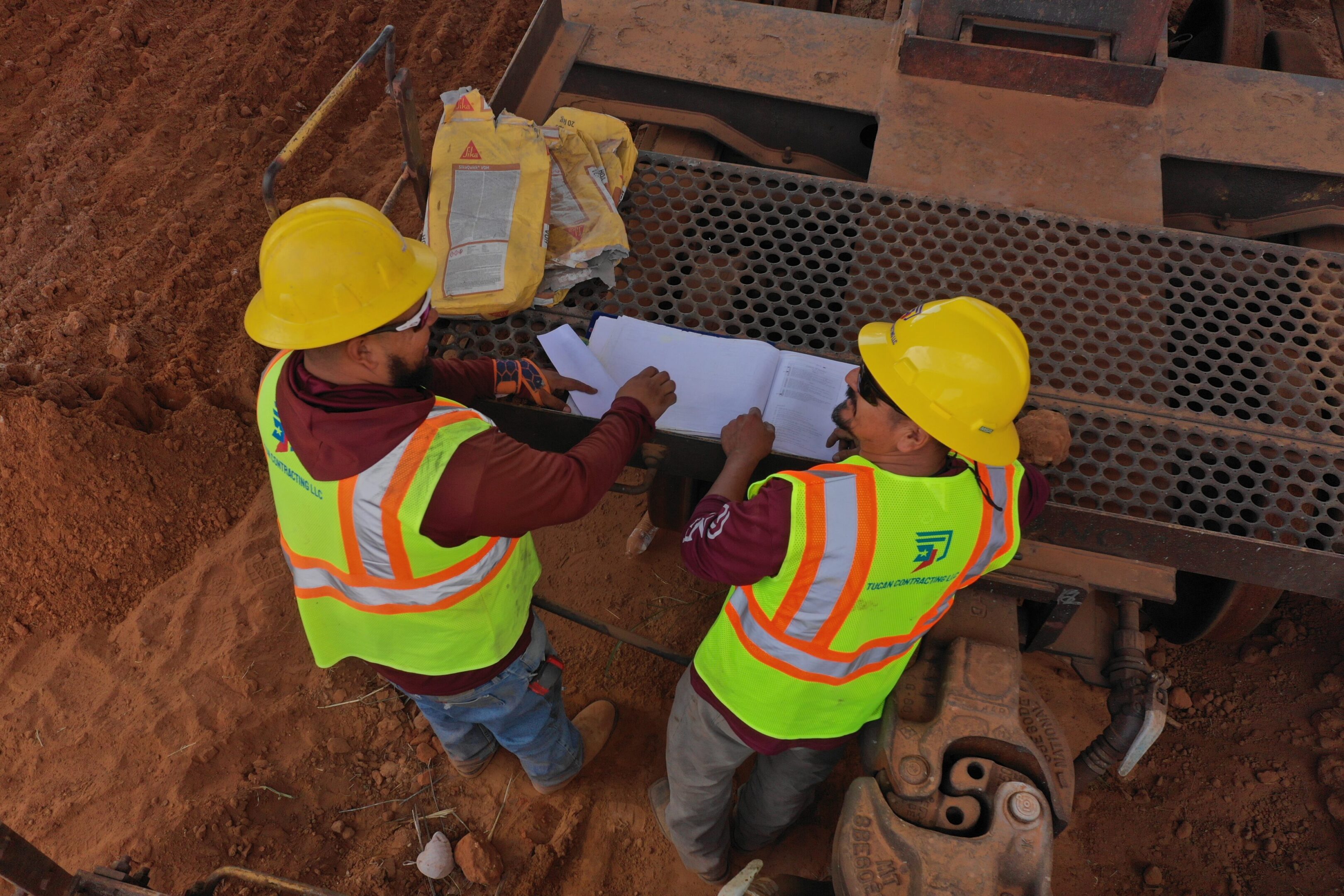 Two construction workers in safety gear reviewing blueprints.
