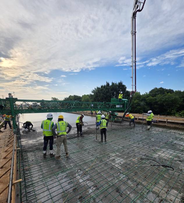 Construction workers pouring concrete on a large slab outdoors.